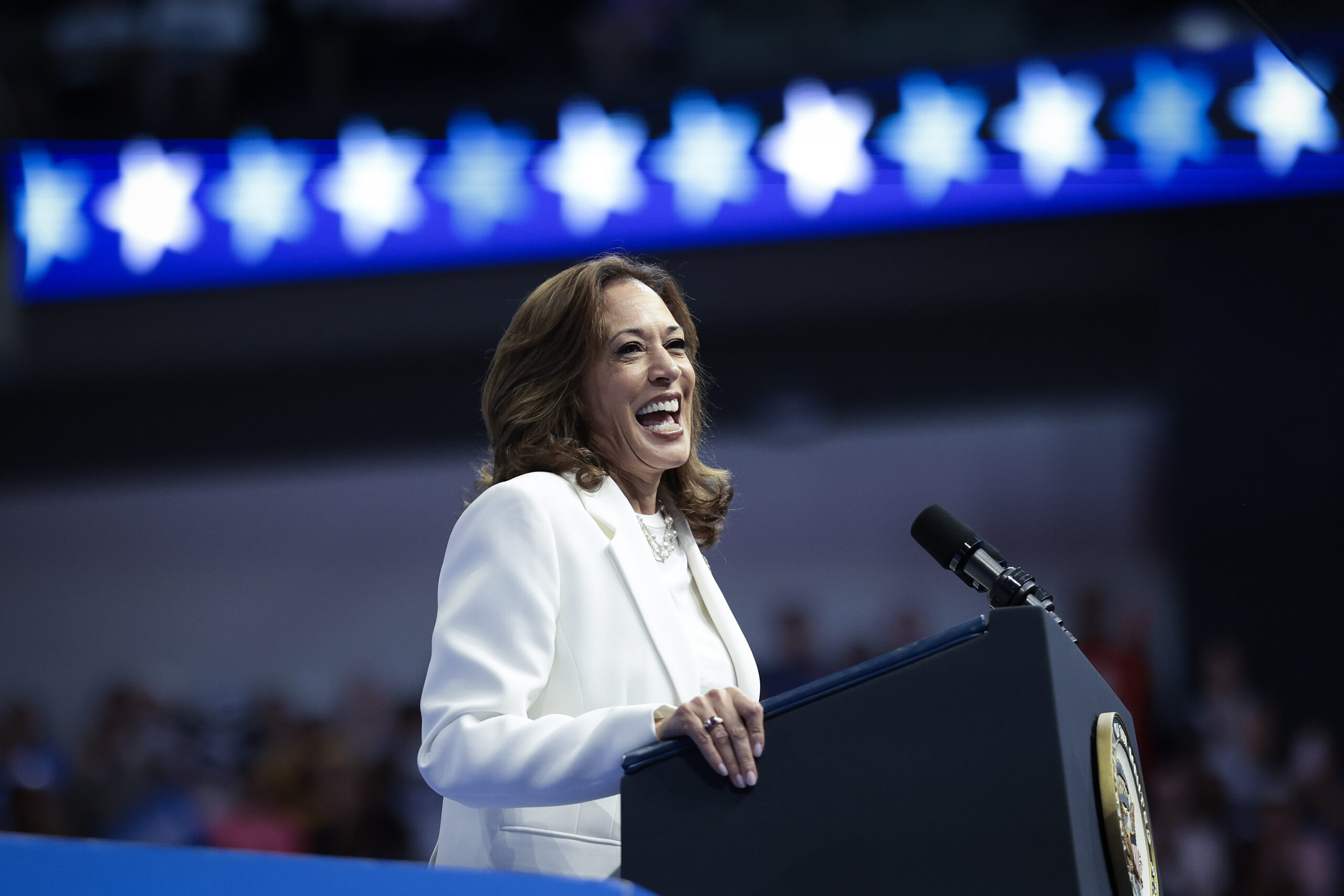 A photo of kamala harris smiling on stage, who currently has election odds to win of -110.