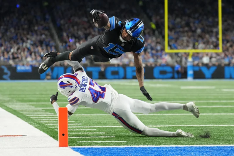 Tim Patrick #17 of the Detroit Lions leaps over Christian Benford #47 of the Buffalo Bills to score a touchdown in the second quarter at Ford Field on December 15, 2024 in Detroit, Michigan. 