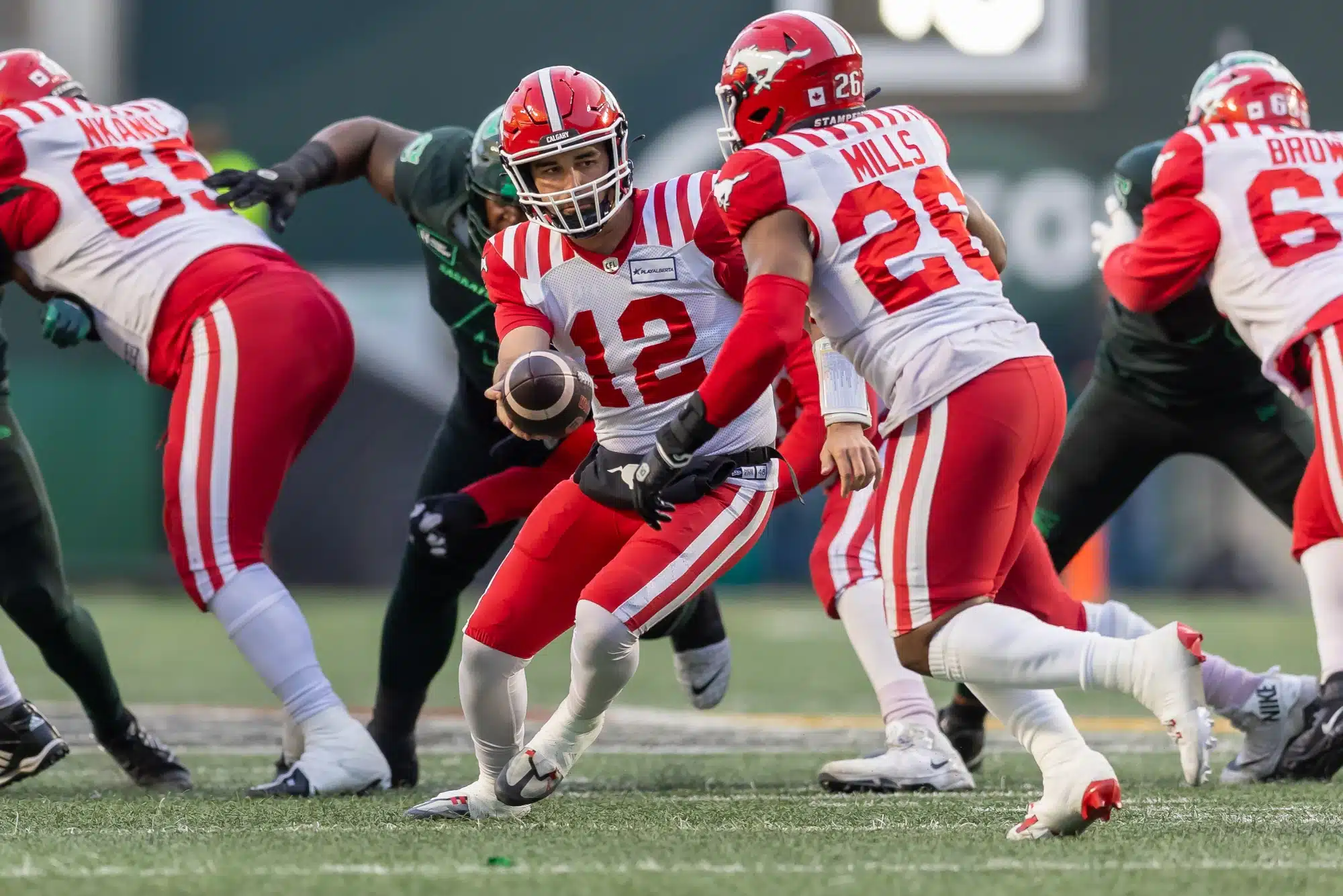 Jake Maier #12 hands the ball off to Dedrick Mills #26 of the Calgary Stampeders in the game between the Calgary Stampeders and Saskatchewan Roughriders at Mosaic Stadium on October 26, 2024 in Regina, Canada.