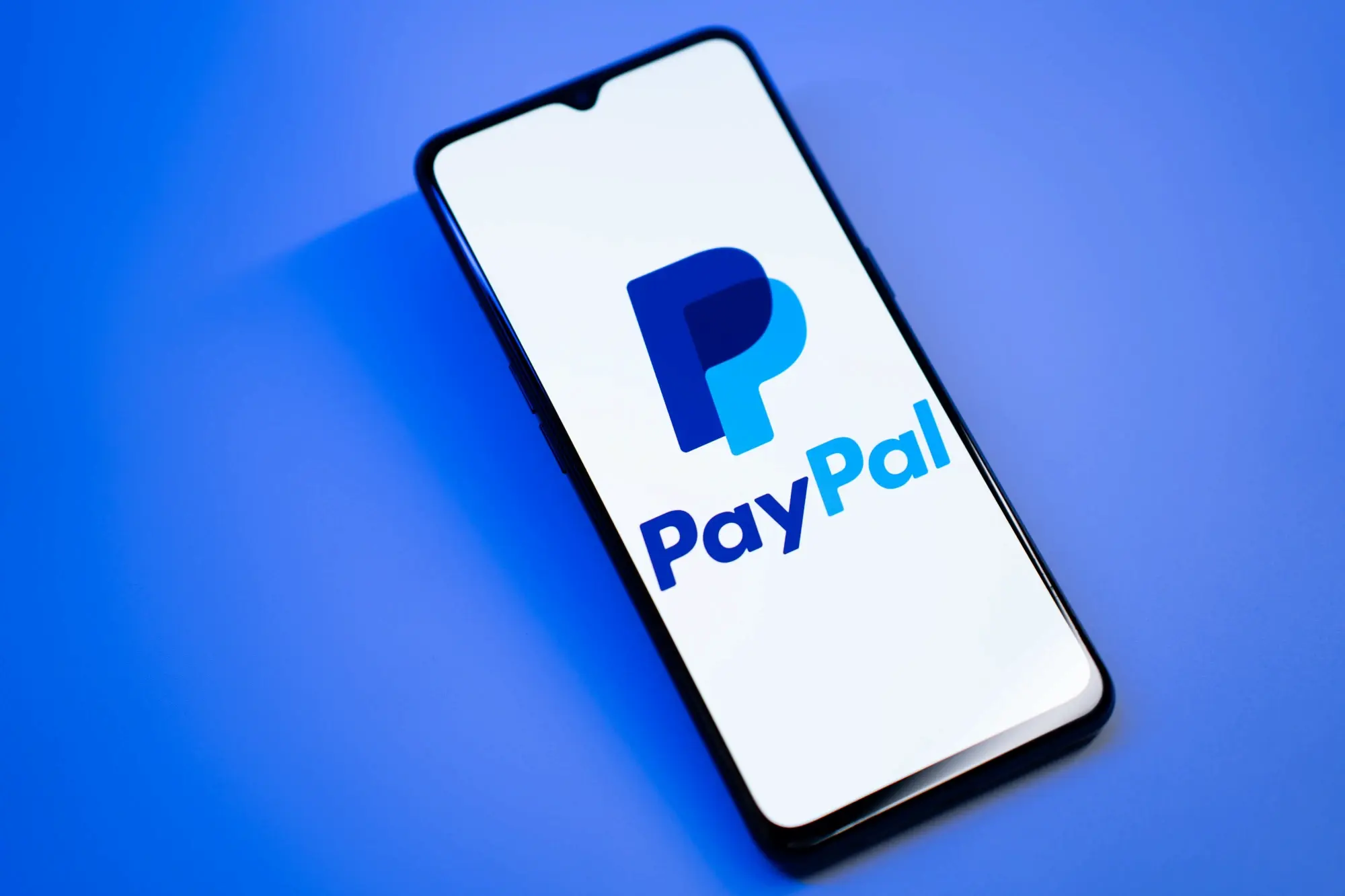 A mobile phone is displaying the logo of the PayPal app on its screen against a blue background.